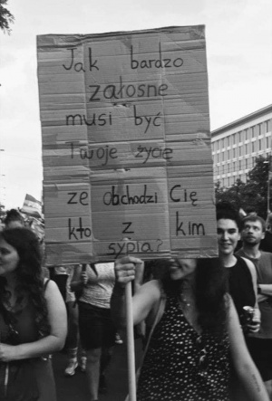 Zdjęcie przedstawia kobietę trzymającą transparent, na którym jest napisane pytanie: Jak bardzo żałosne musi być Twoje życie, że obchodzi Cię, kto z kim sypia?
